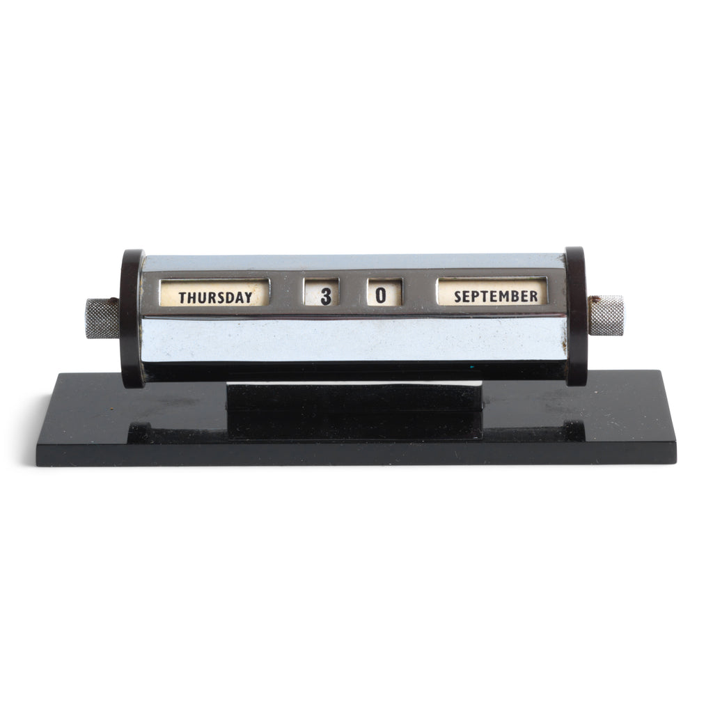 A super-cool 1930s chromium plated perpetual calendar mounted on a black perspex base. The months are adjusted by swivelling the black Bakelite discs either end, and the date is changed by turning the chrome knobs.