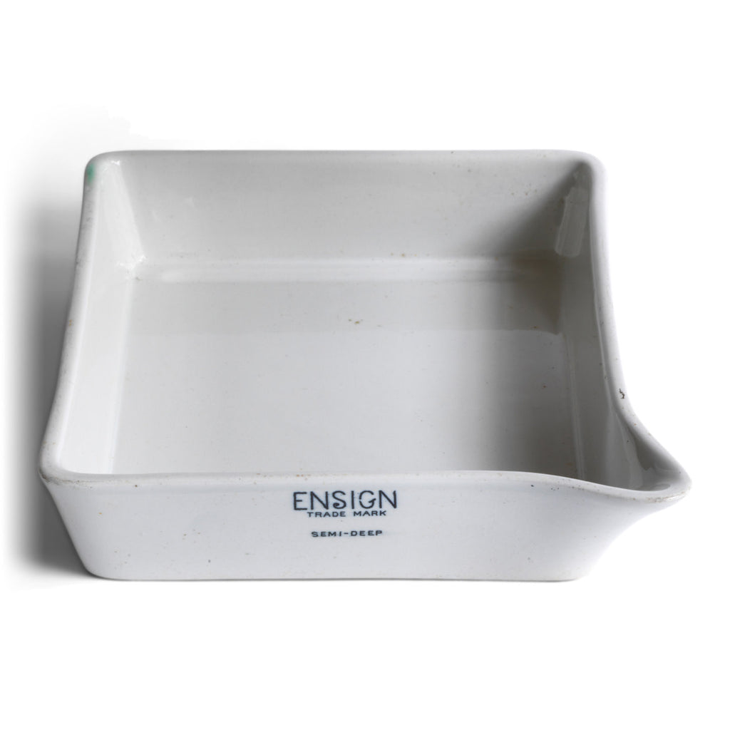 A ceramic ironstone photographic developing tray with pouring lip, made by Ensign, a Victorian manufacturer of porcelain darkroom products. Today it can be repurposed for kitchen use, or as a stand for plants. The makers stamp can be seen on the front end of the tray.