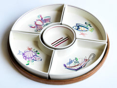 A very striking and rare mid century vintage Poole Pottery seafood hors d'oeuvre set consisting of five ceramic dishes that fit snugly into a circular wooden tray. Each crescent shaped dish is decorated with a hand painted pattern of a shrimp, a flatfish, a crab and a scallop - designed by Truda Carter and hand painted on Poole Pottery's  alpine white glaze. Each piece is stamped to its underside "Handmade Hand Decorated Poole England", along with the paintress's mark.