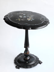 A particularly splendid Victorian black laquered wood and papier-mâché tilt-top parlour table. The beautiful ovoid shaped table top is covered in painted abstract florals and inlaid with shards of mother of pearl, and it is hinged, with an under catch, so that it can easily be stored on one side. It is carried on a single turned pedestal with flaring base which is mounted on three metal webbed feet.