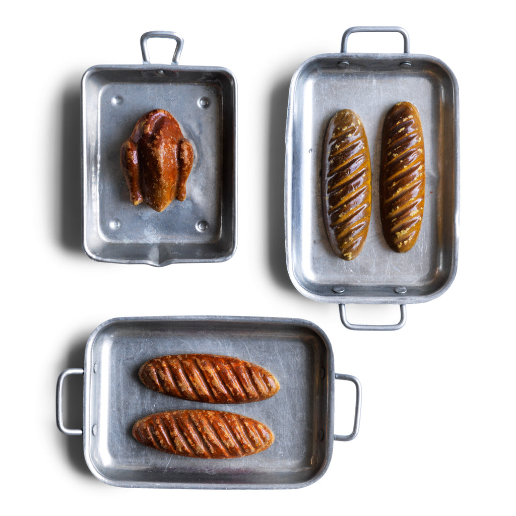 A charming collection of vintage doll's house bloomer style loaves with slashed baked tops; a set of aluminium baking / roasting pans with handles; and a fat little burnished roast chicken - all with their original painted finish, and modelled from a composition plaster material.