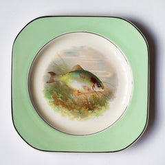 A fish pattern plate, and part of a glorious 1930s fish dinner service, complete with a large platter for serving a whole fish.  Each piece is embellished with a fresh water fish, such as pike, perch and trout, and contained within a mint-green border. Each item is stamped "Woods Ivory Ware England" to its underside.