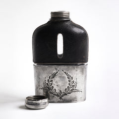 A quality Edwardian silver plated, glass and black leather hip flask with a screw-cap top, and beautiful leaf decoration etched into the silver plate. The clear glass body is half covered with leather, the lower half has a detachable silver plated cover that also acts as a cup.