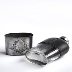 A quality Edwardian silver plated, glass and black leather hip flask with a screw-cap top, and beautiful leaf decoration etched into the silver plate. The clear glass body is half covered with leather, the lower half has a detachable silver plated cover that also acts as a cup.