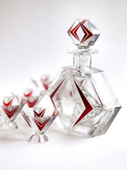 A stunning and rare Art Deco etched black and ruby glass decanter set designed by Karl Palda c.1930. The set comprises of a decanter with stopper and six conical shaped facet cut glass cocktail glasses, each with a flaring foot. Each piece is decorated with Art Deco geometric florals and red chevrons.