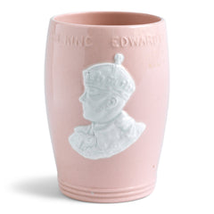 An Edward VIII coronation beaker with pink and white glaze by Johnson Brothers, made to commemorate the king that was never actually crowned. "H M King Edward VIII Coronation 1937" is raised in relief near the rim, and its form with ribbed foot is typical of the 1930s modernist movement prevailing at the time. A portrait of Edward VIII and "E R" decorate the main body of the beaker.