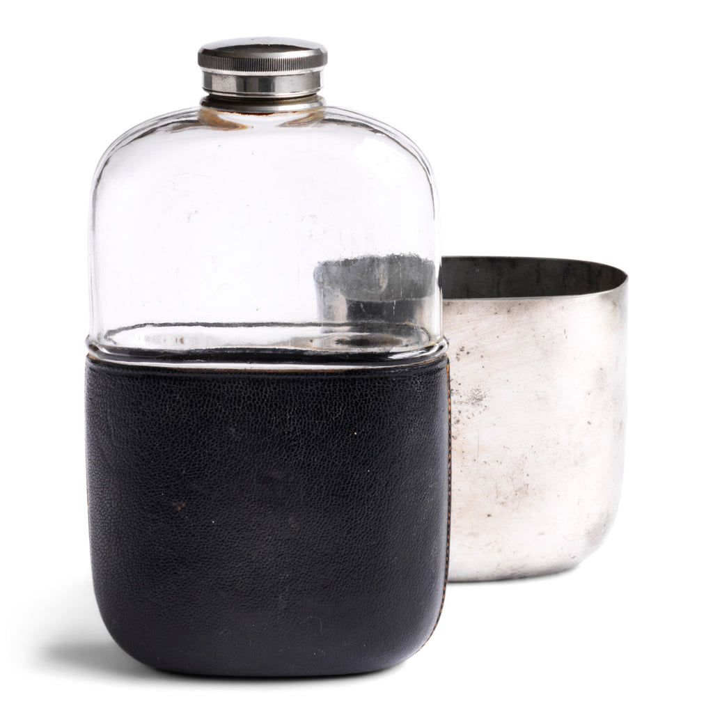 An Edwardian silver plated, glass and black leather 1/2 pint hip flask with a screw-cap top by "James Dickson & Sons Sheffield". The clear glass body is half covered with leather, the upper half has a detachable silver plated cover that also acts as a cup.