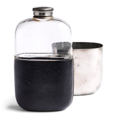 An Edwardian silver plated, glass and black leather 1/2 pint hip flask with a screw-cap top by "James Dickson & Sons Sheffield". The clear glass body is half covered with leather, the upper half has a detachable silver plated cover that also acts as a cup.