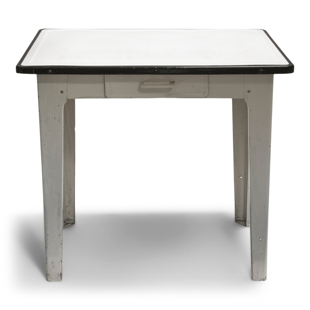 A good-looking mid-century enamel topped kitchen table. The white enamel top has a black enamel rim, and is carried on an off-white painted steel frame fitted with a single drawer and tapering steel legs.