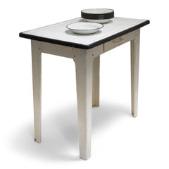 A good-looking mid-century enamel topped kitchen table. The white enamel top has a black enamel rim, and is carried on an off-white painted steel frame fitted with a single drawer and tapering steel legs.