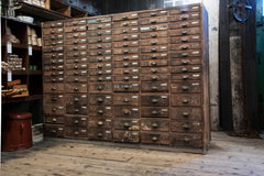 An exceptional bank of antique wooden workshop drawers with original patina and finish. Each of the 90 drawers has a cup-shaped metal pull handle and a name-plate holder; the lower, deeper drawers are singular inside, whereas the upper slimmer drawers contain divisions.