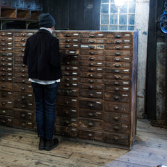 An exceptional bank of antique wooden workshop drawers with original patina and finish. Each of the 90 drawers has a cup-shaped metal pull handle and a name-plate holder; the lower, deeper drawers are singular inside, whereas the upper slimmer drawers contain divisions.