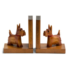 A charming pair of 1930s carved wood scottie dog bookends. Each dog has a painted red collar and tongue, and is mounted on an oak platform with an oak support modelled as a book. Scottie dogs were all the rage in the 1930s: as pets with box-clipped muzzles; as stylised Art Deco Bakelite brooches and clasps; adorning greetings and postcards; as ornaments, modelled in china, metal and wood; and as bookends - such as this dear little pair.