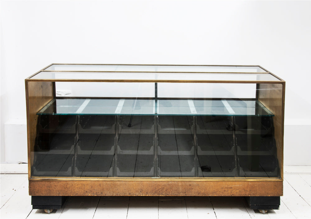 A rare high quality 1930s Art Deco shop counter fitted with eighteen Bakelite display drawers and brass frame to its vitrine. It has oak veneer panelled sides and front with black painted Art Deco stepped feet mounted on ball castors – so it can be moved with absolute ease.  The maker and shopfitters nameplate ‘Courtney Pope Ltd of London N15’ is secured to the inside front of the cabinet, and each Bakelite drawer is beautifully monogrammed with the initials CP in a striking 1930s modernist font.