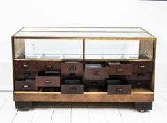 A rare high quality 1930s Art Deco shop counter fitted with eighteen Bakelite display drawers and brass frame to its vitrine. It has oak veneer panelled sides and front with black painted Art Deco stepped feet mounted on ball castors – so it can be moved with absolute ease.  The maker and shopfitters nameplate ‘Courtney Pope Ltd of London N15’ is secured to the inside front of the cabinet, and each Bakelite drawer is beautifully monogrammed with the initials CP in a striking 1930s modernist font.