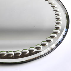 A large and very striking late 19th century tabletop circular mirror with a border of convex fish-eye inclusions, a bevelled edge and a fine metal trim. It has a cream painted back and stands of on three bun feet.