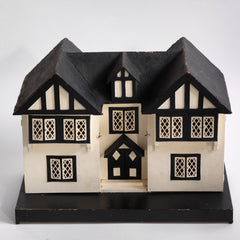 A Tudor style doll's house in the 1930s Mock-Tudor vernacular with twin jettied oriel windows and leaded glass style metal window frames.