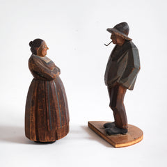 A pair of antique naive wood carved Bavarian peasant figures, one a woman and the other a man with a pipe.