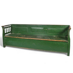 A late 19th century Romanian box bench with its original green painted finish, and a hinged seat that opens to reveal ample storage. It has a panelled back, and its twin arms are supported by turned spindles.