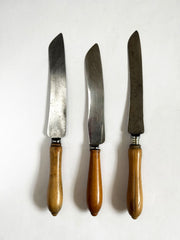 A collection of antique bread knives with carved sycamore and beech handles, and carbon steel engraved blades - two with "Bread" carved on their handles. This image shows the reverse side. 