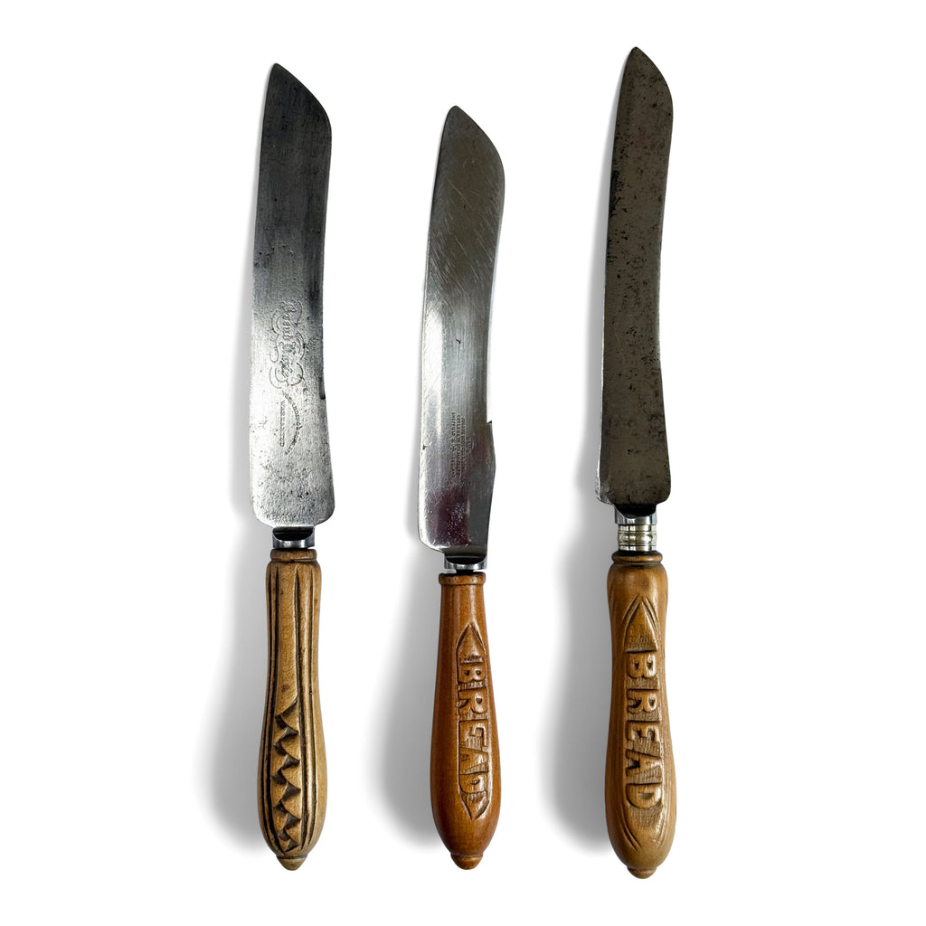 A collection of antique bread knives with carved sycamore and beech handles, and carbon steel engraved blades - two with "Bread" carved on their handles. 