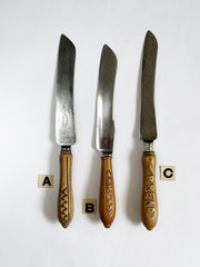 A collection of antique bread knives with carved sycamore and beech handles, and carbon steel engraved blades - two with "Bread" carved on their handles.