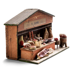 Antique butcher’s shop diorama with its original signage “U. Lamb” and “Family Butcher”.&nbsp; It is complete with counter, papered tiling, butcher’s blocks, butcher’s scales, and various composition cuts, sides and joints of meat – including strings of sausages and a pig’s head.