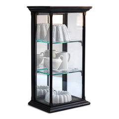 A beautifully proportioned late 19th century table-top ebonised display cabinet with glass on three sides, and with a window of glass on top - so that its contents could be lit from above. It has an elegant plinth base, a top with stepped entablature, and is fitted with three removable glass shelves. The hinged back is fitted inside with a full length mirror that is gently foxed, and it is opened and closed using a brass pull-catch. 