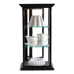 A beautifully proportioned late 19th century table-top ebonised display cabinet with glass on three sides, and with a window of glass on top - so that its contents could be lit from above. It has an elegant plinth base, a top with stepped entablature, and is fitted with three removable glass shelves. The hinged back is fitted inside with a full length mirror that is gently foxed, and it is opened and closed using a brass pull-catch. 