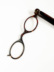 An Edwardian faux tortoiseshell lorgnette - an elegant  pair of fine oval spectacles attached to a long arm in  mock tortoiseshell.