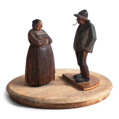 A pair of antique naive wood carved Bavarian peasant figures, one a woman and the other a man with a pipe.