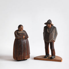 A pair of antique naive wood carved Bavarian peasant figures, one a woman and the other a man with a pipe.
