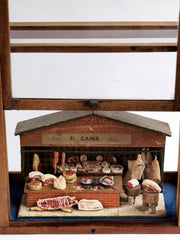 Antique butcher’s shop diorama with its original signage “U. Lamb” and “Family Butcher”.&nbsp; It is complete with counter, papered tiling, butcher’s blocks, butcher’s scales, and various composition cuts, sides and joints of meat – including strings of sausages and a pig’s head.