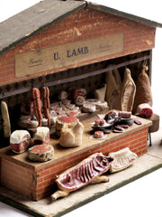 Antique butcher’s shop diorama with its original signage “U. Lamb” and “Family Butcher”.&nbsp; It is complete with counter, papered tiling, butcher’s blocks, butcher’s scales, and various composition cuts, sides and joints of meat – including strings of sausages and a pig’s head.