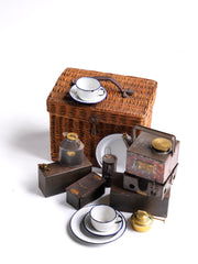 An antique automobilia "En Route" motor car tea basket by Sirram dating to 1910 - 1920: a complete travelling picnic set in white enamel and steel, with brass detailing; each and every carefully designed piece pleasingly housed and stowed in its steel and wicker lined compartments, ready for its travels. The front pulls down to reveal a handy work-station, a fitted vulcanised cardboard tray in racing-car green, where all things for a picnic can be assembled. 