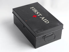 A good-looking first aid tin, the lid stencilled "First Aid" and with a red cross. It has a pair of carrying handles and its original black enamel paint finish.