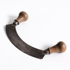 A Victorian kitchen mezzaluna herb chopper with a demilune riveted carbon steel blade and turned beechwood handles.