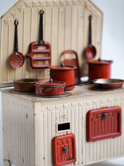 A charming 1930s doll-sized range and with its original cream painted finish and a full set of pots and pans painted in their original ox-blood broawn. The stove back has a pressed tin pattern to its front, along with hooks on its back plate for the hanging of utensils and pans. It also has four removable hob plates, and has an opening oven and also a sliding hot cupboard drawer. 