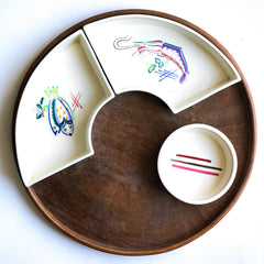 Part of a mid century vintage Poole Pottery seafood hors d'oeuvre set that consists of five ceramic dishes that fit snugly into a circular wooden tray. Each crescent shaped dish is decorated with a hand painted pattern of a shrimp, a flatfish, a crab and a scallop - designed by Truda Carter and hand painted on Poole Pottery's alpine white glaze. Each piece is stamped to its underside "Handmade Hand Decorated Poole England", along with the paintress's mark.