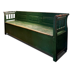 An elegant late 19th century Romanian box bench with its original green painted finish, and a hinged seat that opens to reveal ample storage. It has a panelled back, and its twin arms are supported by turned spindles.