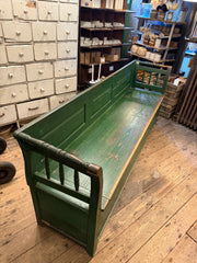 A late 19th century Romanian box bench with its original green painted finish, and a hinged seat that opens to reveal ample storage. It has a panelled back, and its twin arms are supported by turned spindles.
