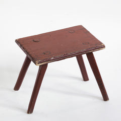 A Romanian folk art small side table or stool with stick legs and with its original brick-red painted finish, and a charming small sheet-metal repair to one corner of its top.