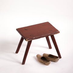 A Romanian folk art small side table or stool with stick legs and with its original brick-red painted finish, and a charming small sheet-metal repair to one corner of its top.