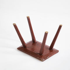 A Romanian folk art small side table or stool with stick legs and with its original brick-red painted finish, and a charming small sheet-metal repair to one corner of its top - showing underside.