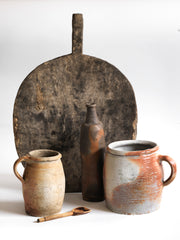 A collection of vintage French rustic earthenware confit pots in grey, beige and brown salt glazes, and a sculptural matt moleskin-brown ceramic calvados bottle. 