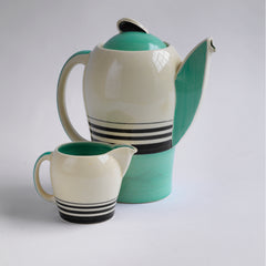 A good 1930s Art Deco Susie Cooper coffee set decorated with green and black banding. Restraint, fitness for purpose and a careful consideration for shape and pattern are Susie Cooper hallmarks, to which this rare 1930s Kestrel shape coffee set in green Tango stands testament. The Susie Cooper trademark 1930s signature leaping deer logo is on the underside of each piece, and the set includes a coffee pot, milk jug, and six coffee cans and  saucers.