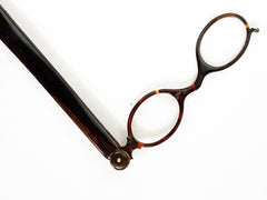 An Edwardian faux tortoiseshell lorgnette - an elegant  pair of fine oval spectacles attached to a long arm in  mock tortoiseshell.