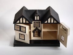 A Tudor style doll's house in the 1930s Mock-Tudor vernacular with twin jettied oriel windows and leaded glass style metal window frames.