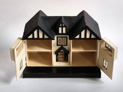 A Tudor style doll's house in the 1930s Mock-Tudor vernacular with twin jettied oriel windows and leaded glass style metal window frames.