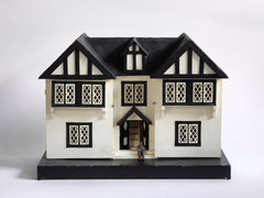 A Tudor style doll's house in the 1930s Mock-Tudor vernacular with twin jettied oriel windows and leaded glass style metal window frames.